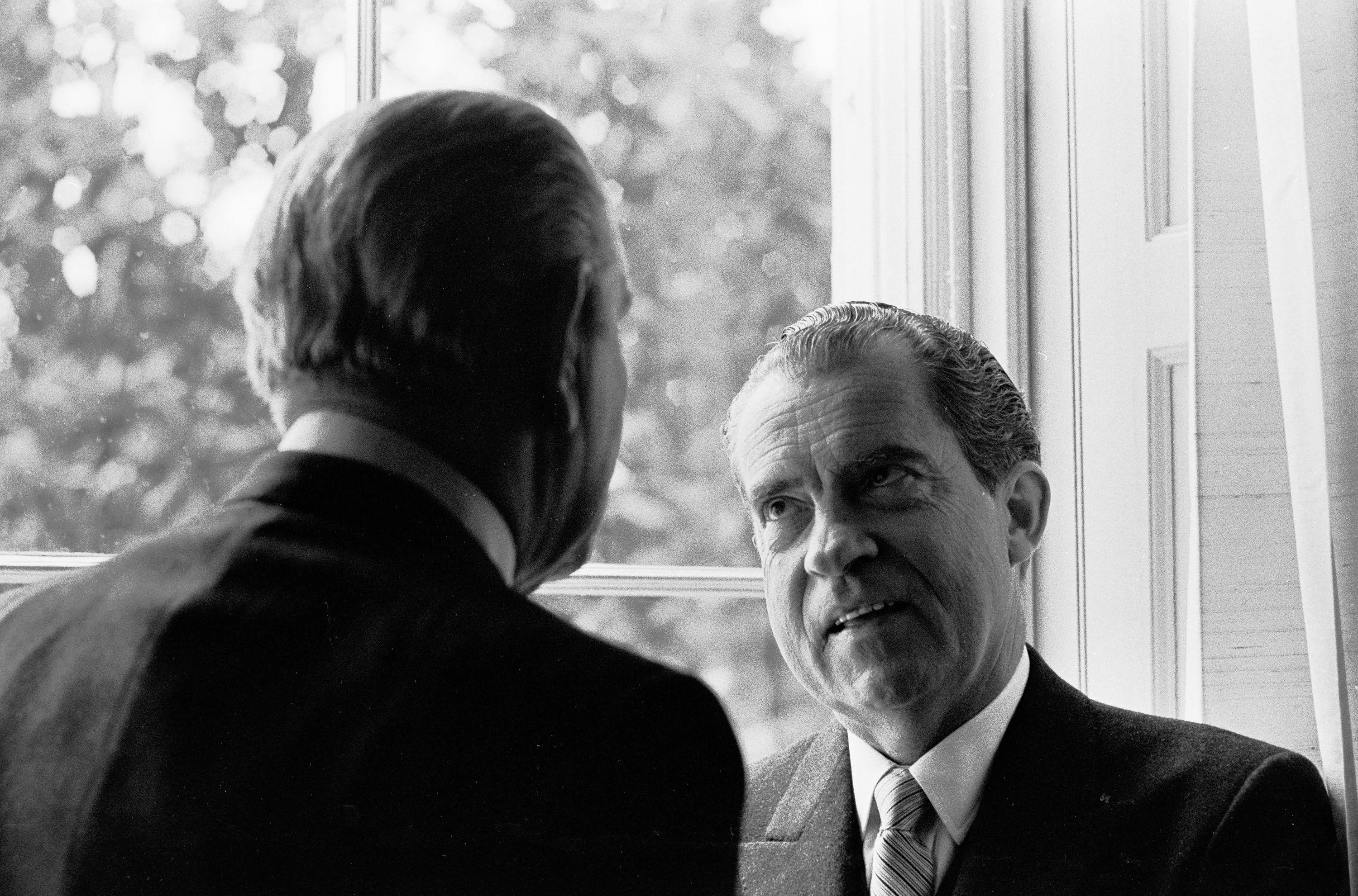 President Lyndon B. Johnson, left, has his back to the camera as he talks to President Richard Nixon in front of a window. 
